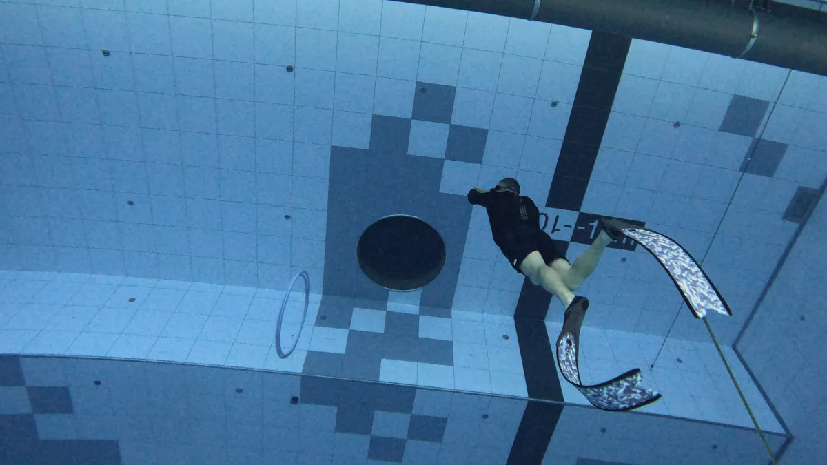 Freediver descending in a deep indoor pool