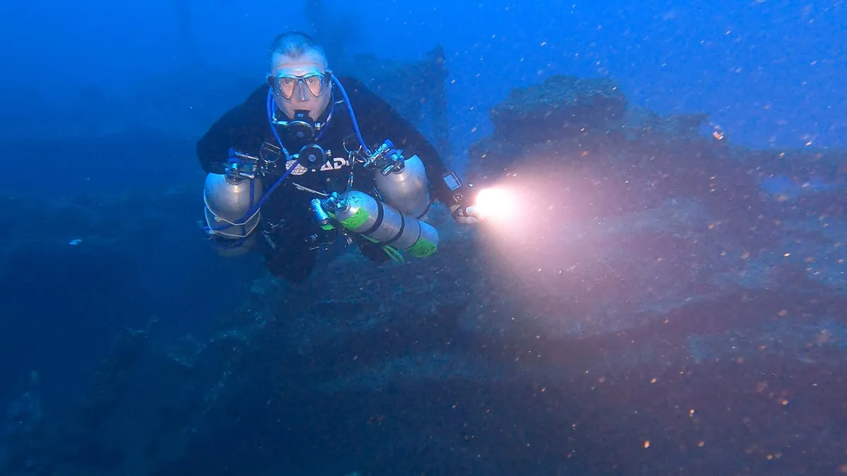 Andrew Grundy scuba diving near wreckage with a torch