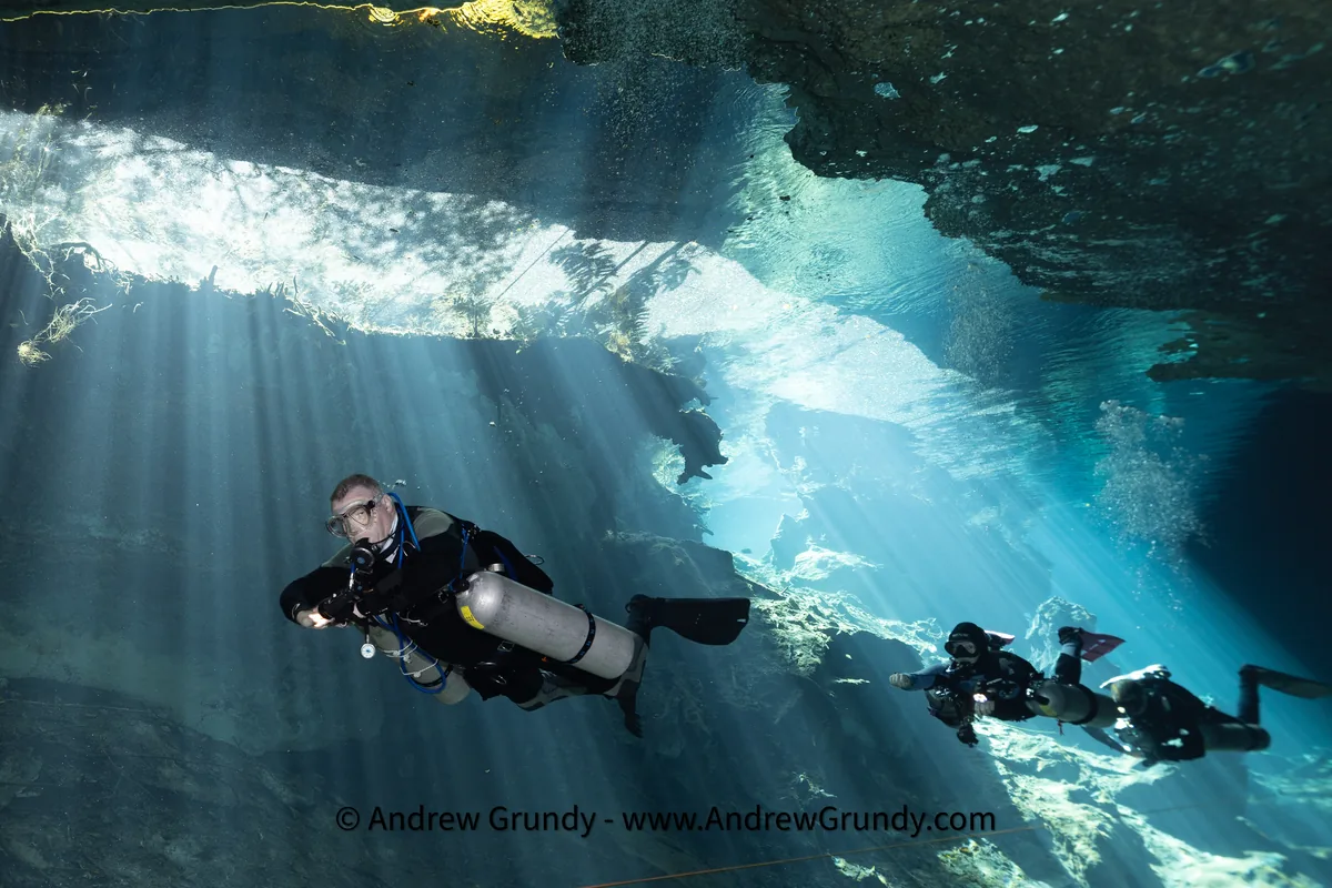 Scuba divers in a cenote with sunlight beams underwater