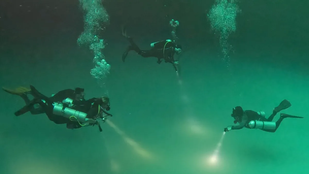 Scuba divers in green UK water using dive lights